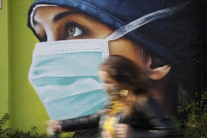 A woman walks in from of a mural of a nurse in Milan.