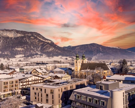 A snowy town at sunset with a twin-spired church and alpine peaks behind