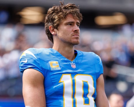 Justin Herbert stands on the sidelines in his blue Chargers jersey, looking to the side