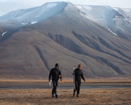 Students walk across tundra checking permafrost depth, with snow-capped mountains behind