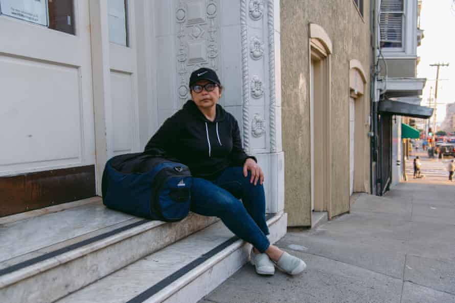 A woman sits on the steps of a building with a dark blue duffel bag at her side.