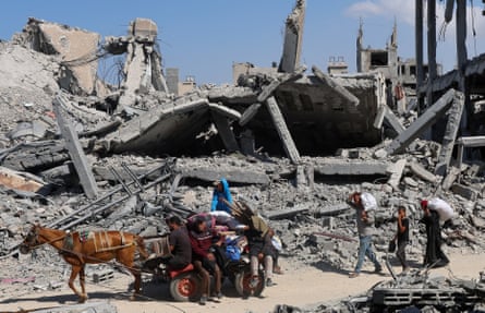 A horse pulls a cart carrying people and their belongings past the rubble of destroyed buildings.