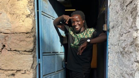 Maasai musician Jeyster Music, smiling at the door of a stone building.