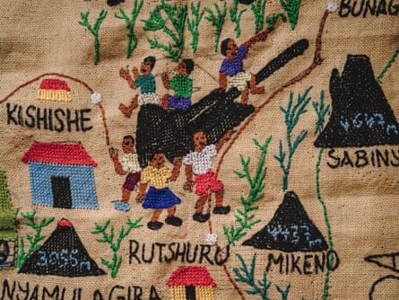 A embroidered artwork with the names of towns and volcanoes in North Kivu sewn on it. Some people sit on what looks like a cannon.