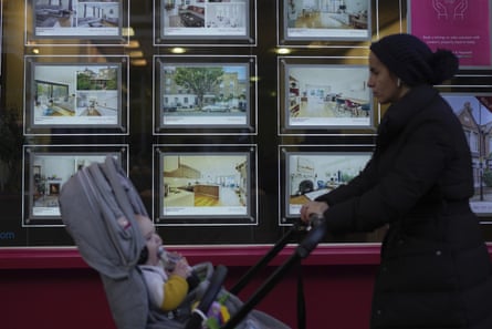 A woman pushing a baby in a pushchair walks past an estate agent’s window