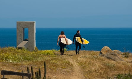 Two male surfers wearing wetsuits walking down a dirt path with surfboards to surf Punta de Lobos, Pichilemu, Chile.