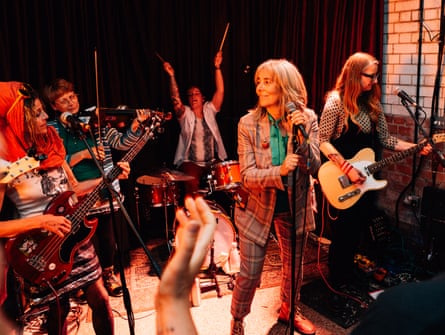 A band of women jamming, looking at each other as the drummer lifts her sticks high in the air