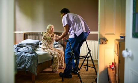 Young male care worker helping woman off bed with walking frame nearby