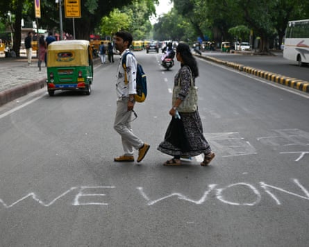 Pedestrians cross a busy street near Jantar Mantar in New Delhi, India. On the road, the words “WE WON” are written in white chalk graffiti.