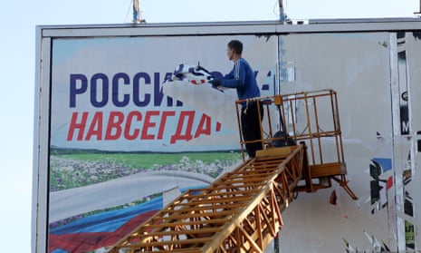 A worker tears away a billboard reading “Russia is here forever”.