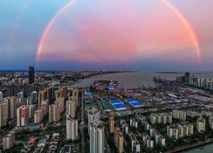 The perfect arc of a pinkish-hued shining rainbow pictured above a wide urban landscape