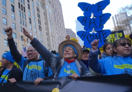 Older women in blue shirts march holding banner and raising fists.