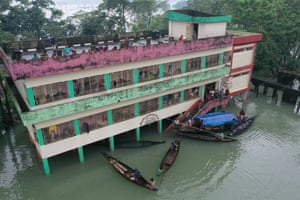 People stand on balconies and on the roof of a school as boats pull up to the stairs
