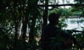 Silhouette of a man sitting in shade of trees by a river