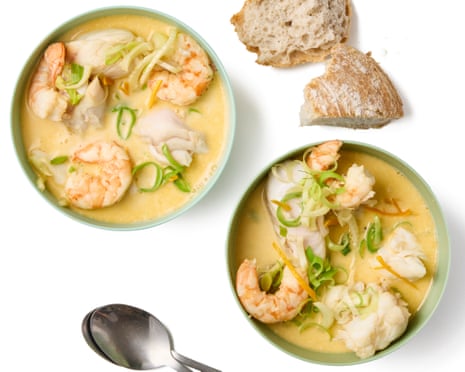 Two bowls of creamy fish stew with shrimp and vegetables, alongside bread and a bowl of sauce.