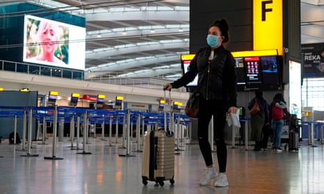 A traveller wearing a face mask walks with her luggage in the departures hall at Heathrow Terminal 5
