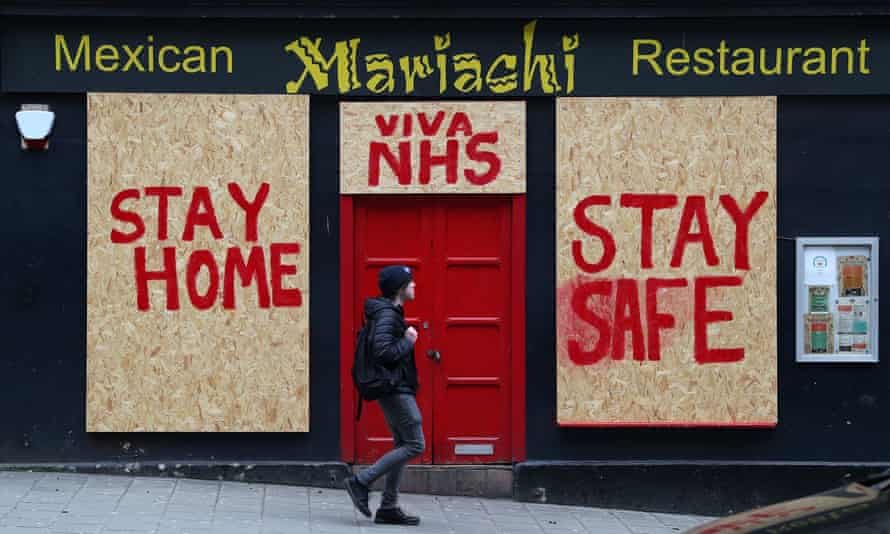 A person passes a boarded up restaurant in Edinburgh which has been painted with an NHS supporting message.