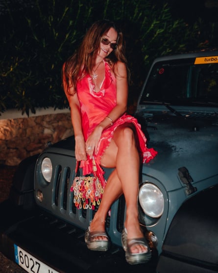 In a vivid red dress, she sits on the bonnet of a Jeep at night