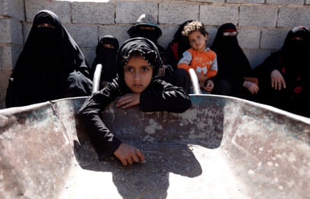 People, mostly women and children, wait for food aid in Sana’a, Yemen, with a young girl leaning into an empty serving vessel and facing the camera looking sad.