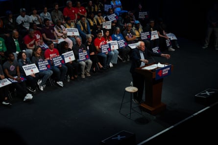 a man speaks into a microphone astatine a lectern while rows of group beryllium down him holding pro-union signs