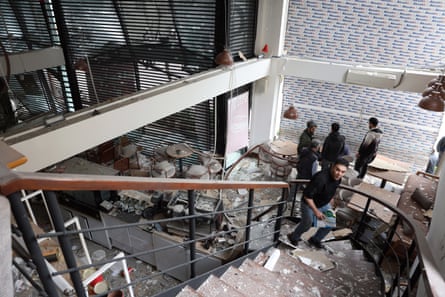 People stand at the bottom of a staircase in a cafe, with wreckage strewn across the floor