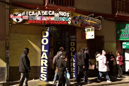People walking past a billboard outside a currency exchange shop in La Paz, Bolivia