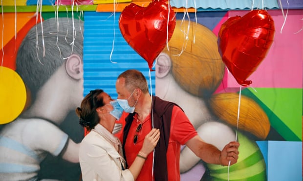A couple wearing protective face masks hold heart-shaped red balloons in Paris, France. 