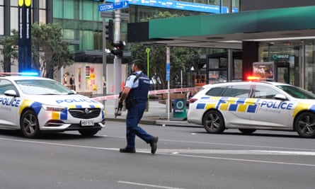 An armed police officer walks in a street between police cars in Auckland