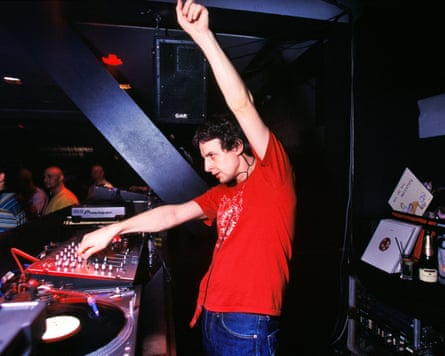 Man in a red T-shirt with left arm aloft djing