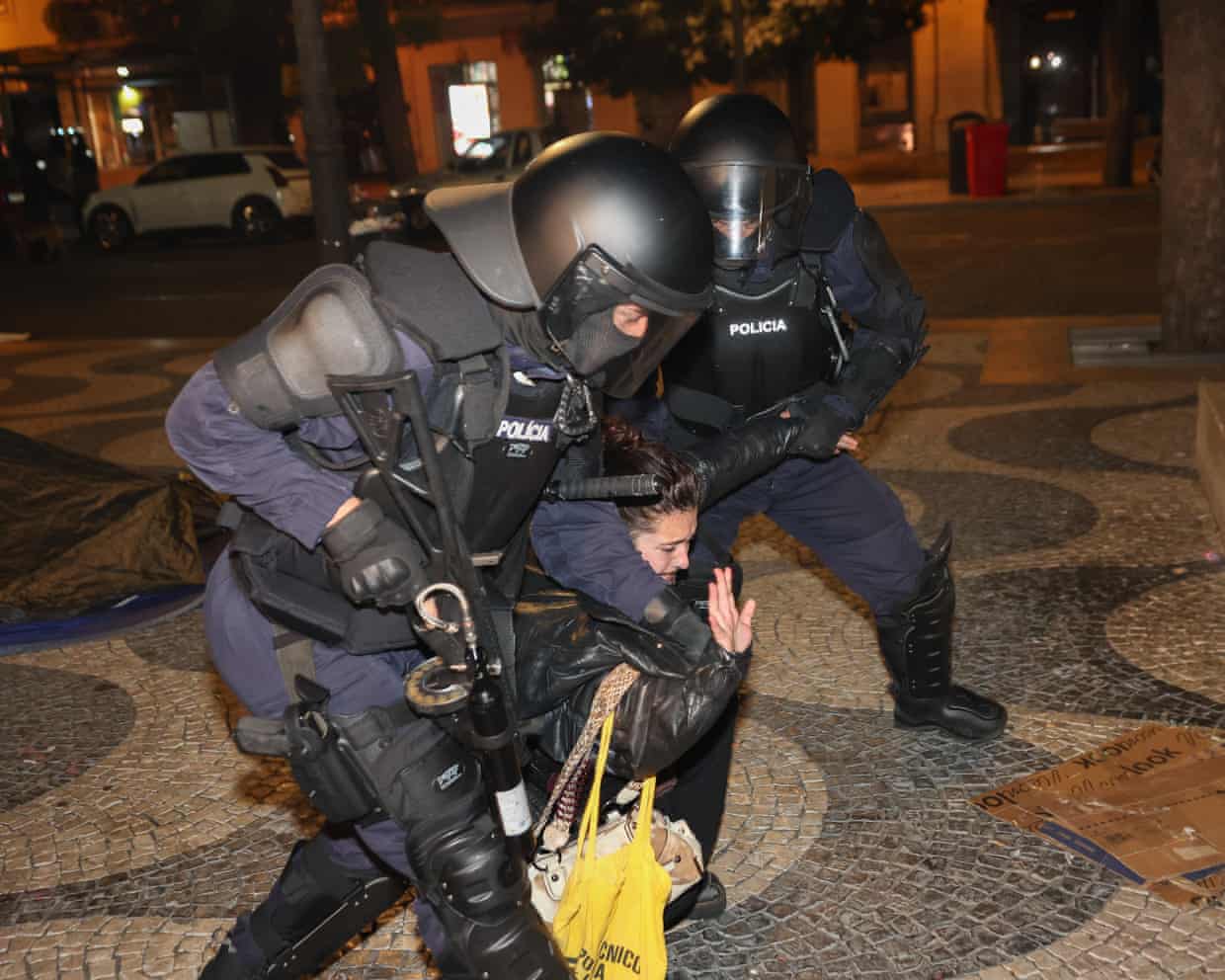 Two police officers in riot gear drag a woman away