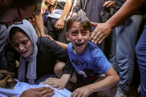 A young boy in a pale blue T-shirt cries over the body of a man as other surround the deceased