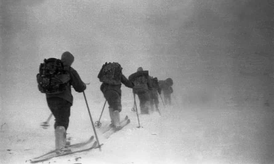 A line of people on skis amid mist and darkness