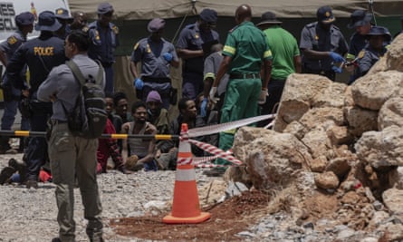 Men sit on the ground surrounded by police and rubble.