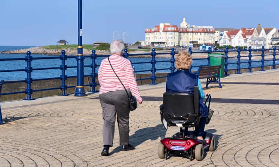Two elderly women on a promenade: one walking and one riding a mobility scooter