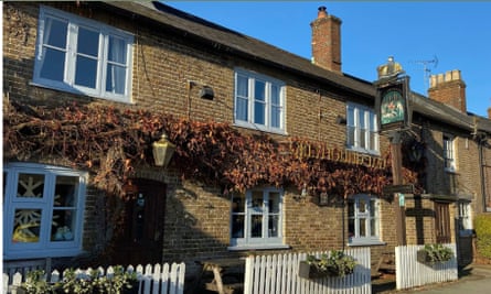 The exterior of the Greyhound Inn, it is a brick building with a white picket fence, it is a sunny day with autumn leaves on the vine that spans the pub