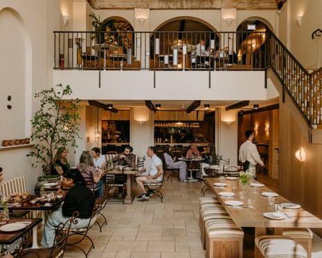 Interior of Kinz London restaurant, showing a two-level dining room with diners at tables. Caption reads: ‘There’s something cinematic about this elegantly staged setting.’