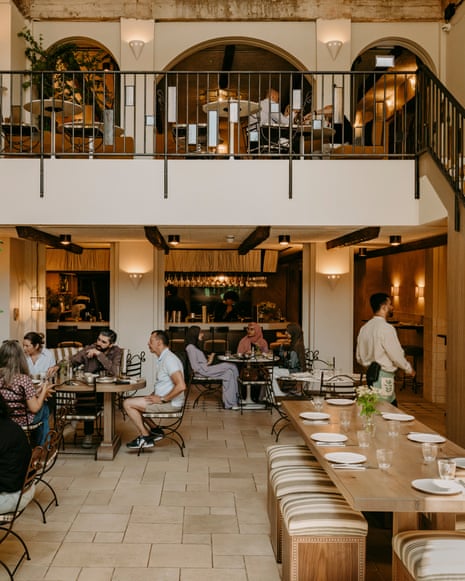 Interior of Kinz London restaurant, showing a two-level dining room with diners at tables. Caption reads: ‘There’s something cinematic about this elegantly staged setting.’