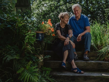 A man in a blue top and a woman in a stripy top and a black vest, sitting on steps in a garden