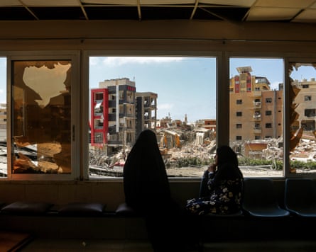 Women look from a window of the damaged hospital on to ruins outside
