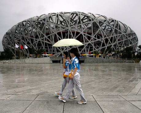 Des piétons sous la pluie passent devant le Stade olympique national de Pékin, en Chine.