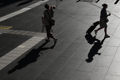 Two people covered in shadow walk on a sidewalk.