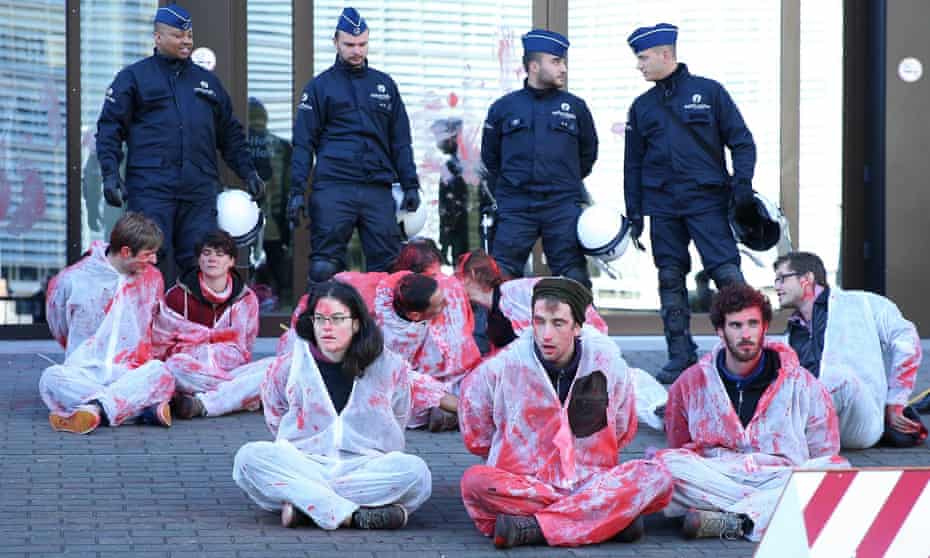 Police stand guard as activists wearing suits covered in fake blood take part in protests against the Comprehensive Economic and Trade Agreement (Ceta) in front of the EU council building in Brussels on 30 October.