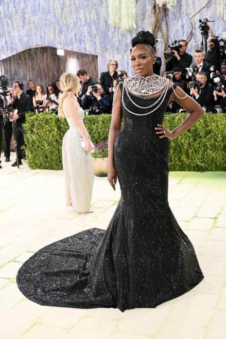 woman in black dress and statement necklace poses with hand on hip