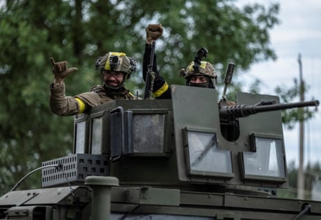 Ukrainian service members gesture as they ride an armoured vehicle in the town of Vovchansk, in Kharkiv.