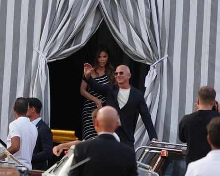 Jeff Bezos waves to onlookers from outside a hotel, with his fiancee, Lauren Sanchez, behind him.
