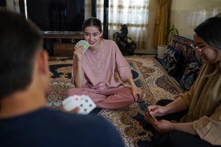 Three people sit on a rug playing cards.