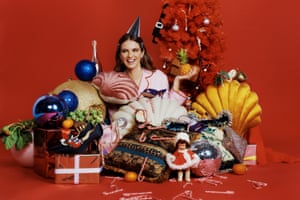 A smiling model surrounded by Christmas gifts, with baubles and tinsel and a red background