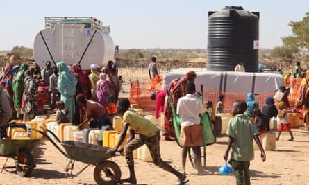 African children and adults, most with short hair and wearing colorful hot-weather clothing, gather around a truck with a white back on it.