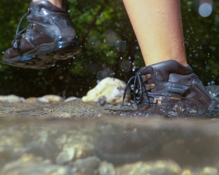 An unrecognisable woman hiking on a sunny day steps out of a glassy river