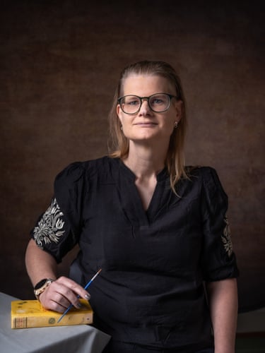 A woman holds a small brush and rests her hand on a book